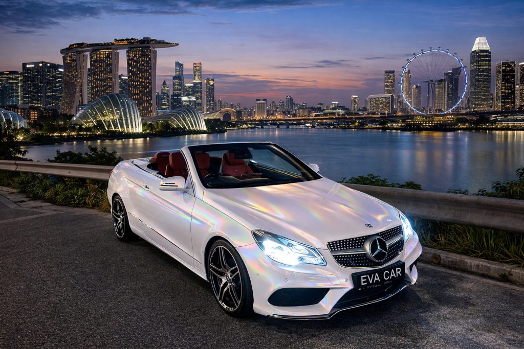 White Mercedes E-Class cabriolet at Marina Bay at dusk, the model behind Eva Car Rental's cabriolet rental Singapore service.